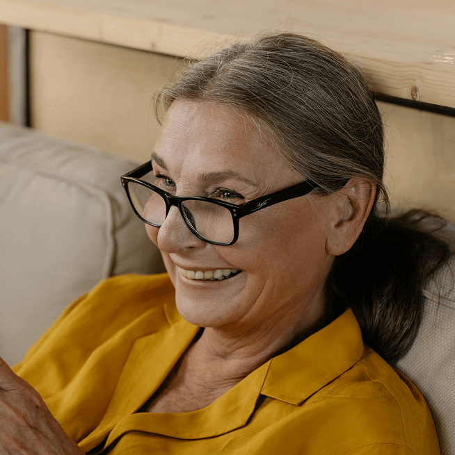 Close-up, circular photo of an older woman with a broad, genuine smile, wearing glasses, and looking towards the upper right.